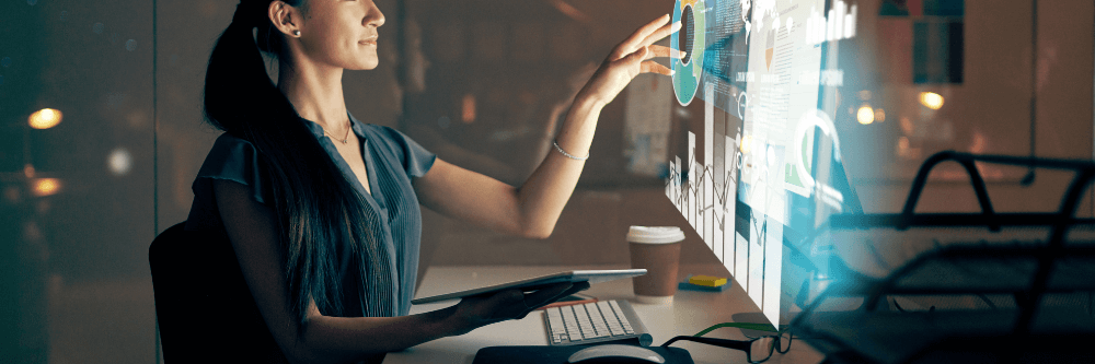 Woman sitting at a desk manipulating data on a futuristic screen.
