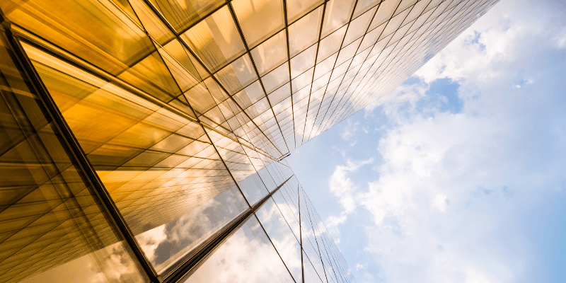 Gold colored windows on an office building next to a blue cloudy sky