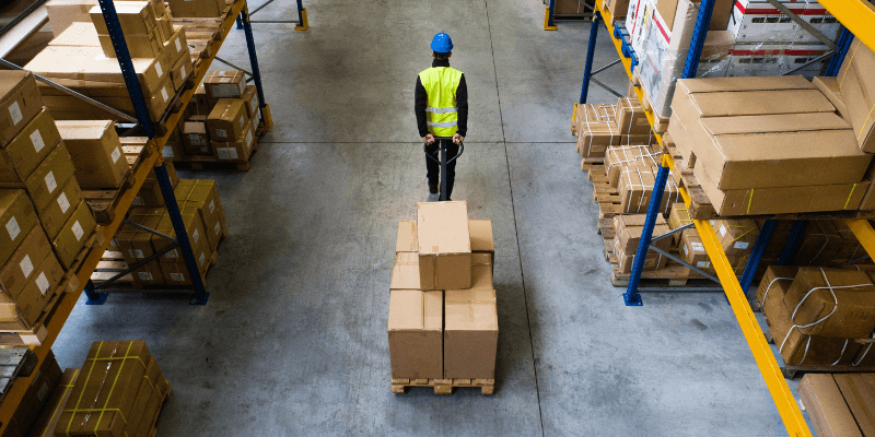 man working in a logistical warehouse pulling a cart