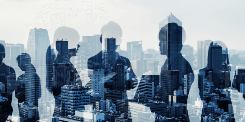 The outline of business people overlaid over a city skyline, blue tint