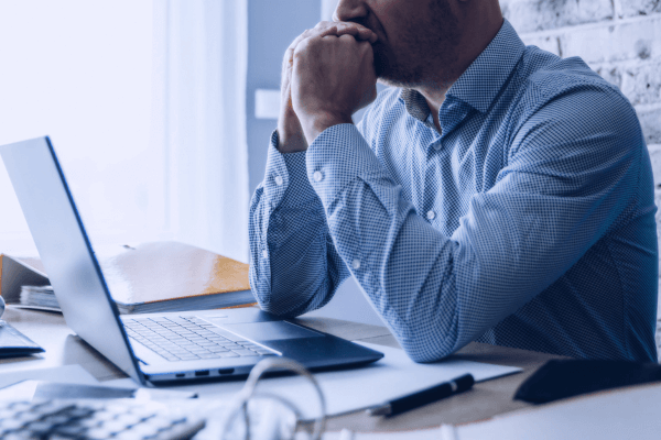 Businessman in a blue shirt with a laptop. He appears to be overwhelmed or concerned about some information on his laptop.