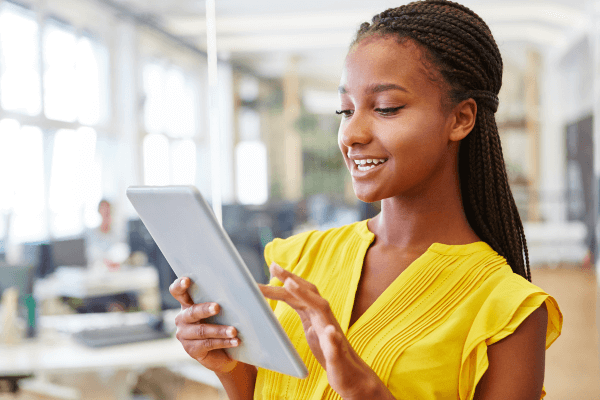 Woman in a yellow blouse working on a tablet while in the office.