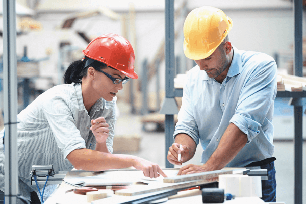 2 employees in a manufacturing setting looking over documents and plans 